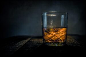 A glass containing a measure of a dark spirit, either rum or whisky on a black background